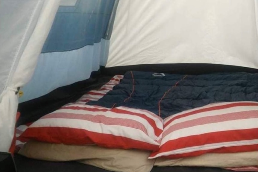 A sleeping bag and two pillows make  bed in the tent of a homeless person. 
