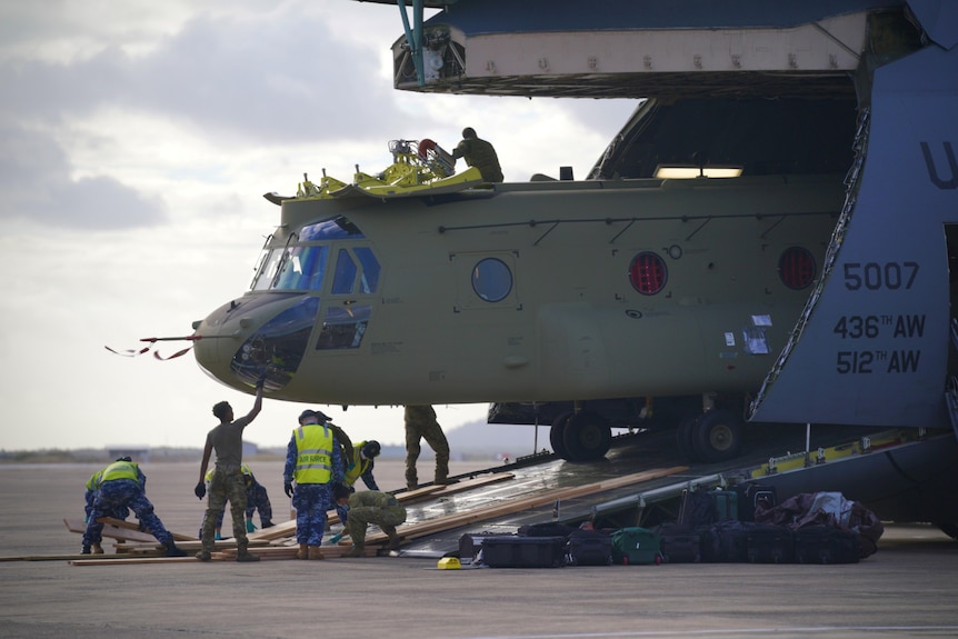 A Chinook is unloaded from the open nose of a large US military cargo plane.