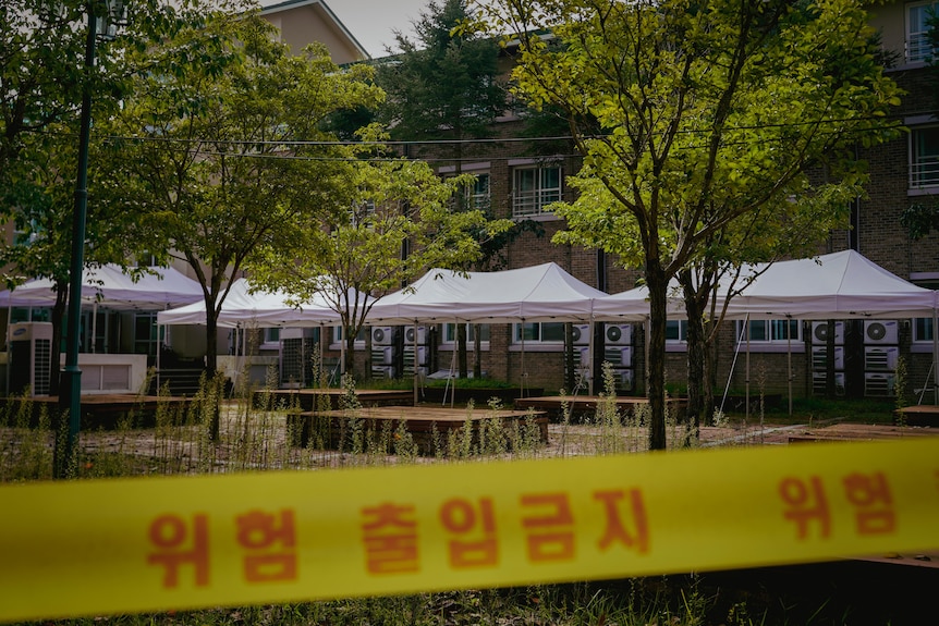 Yellow warning tape with a message in Hangul is strung up outside a building.  White party tents have also been erected outside