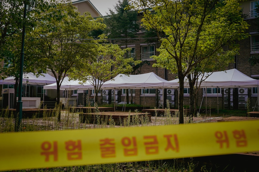 Yellow caution tape with a message in Hangul is strung up outside of a building. White marquees have also been erected outside