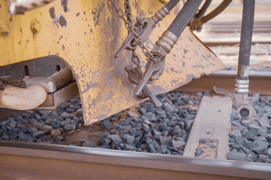 A closer look of a yellow underside slightly rusted freight train. Tracks can also be seen