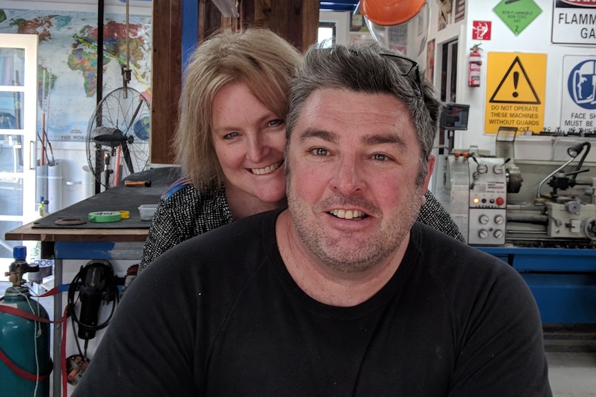 A middle-aged man and woman in a garage full of tools and machinery. 