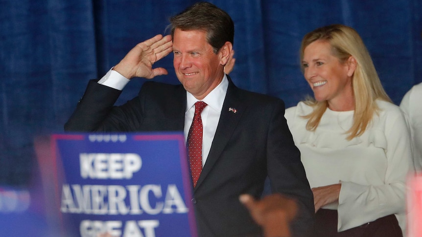 Georgia Governor Brian Kemp salutes as he stands next to his wife Marty.