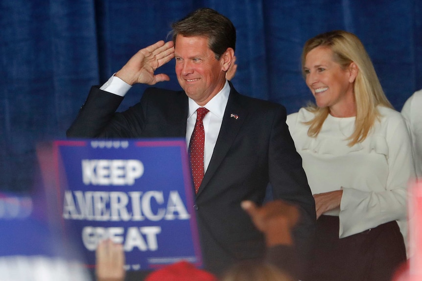 Georgia Governor Brian Kemp salutes as he stands next to his wife Marty.