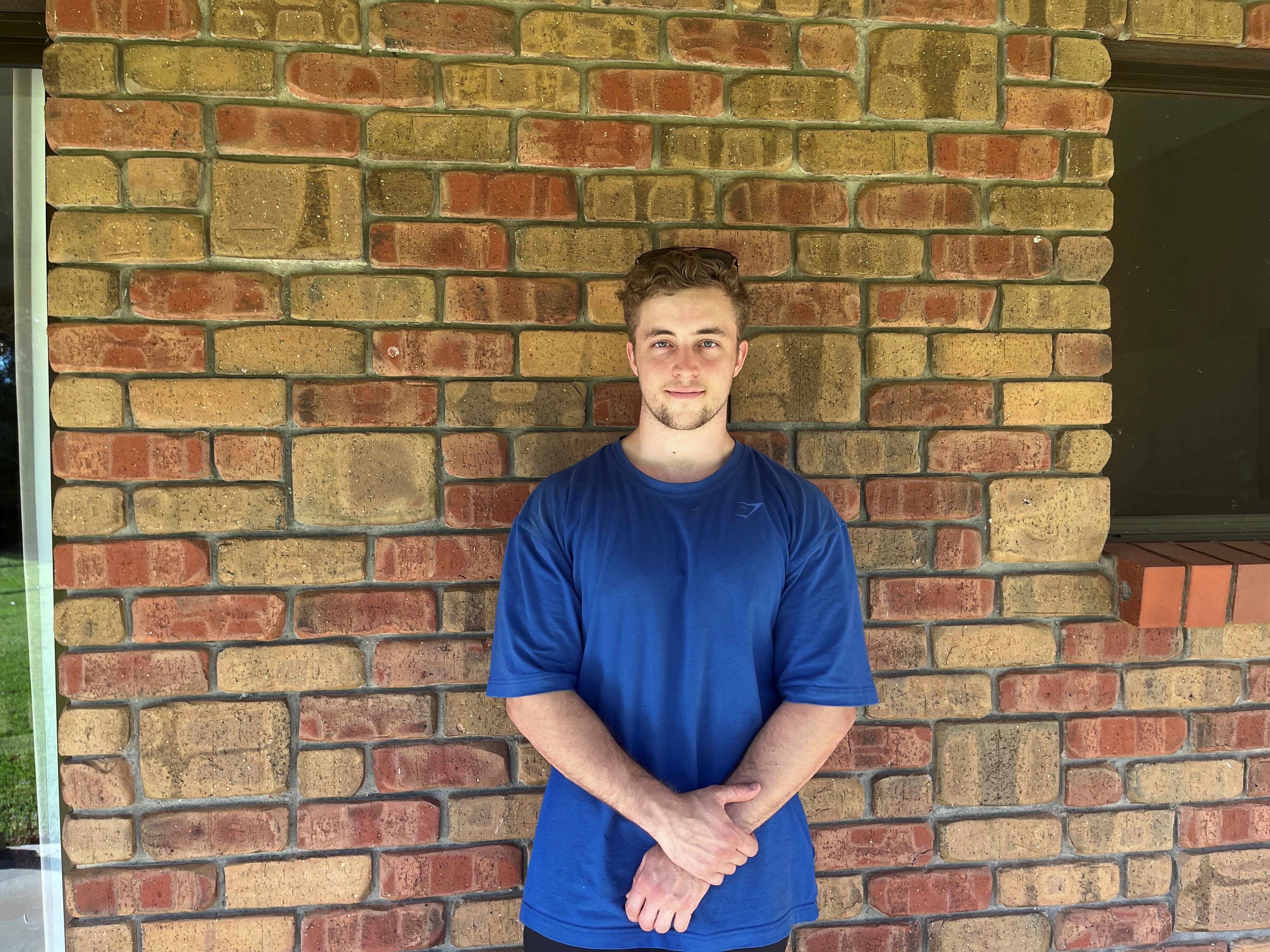 a young caucasian man in a blue shirt standing in front of a brick wall