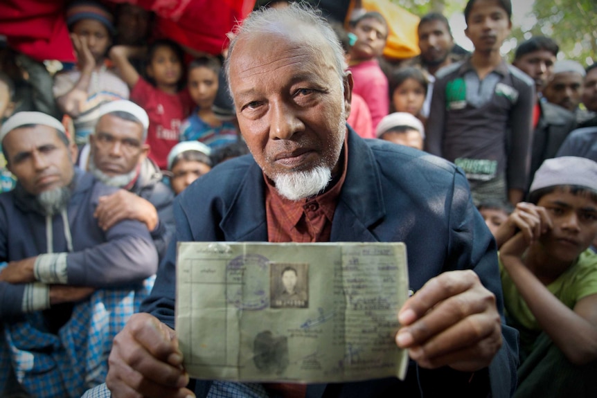 A man holds a national registration card with a crowd of people behin him.