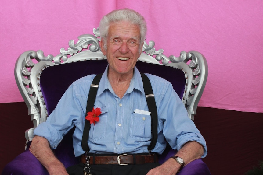 An elderly man, sitting on a silver throne, smiling.