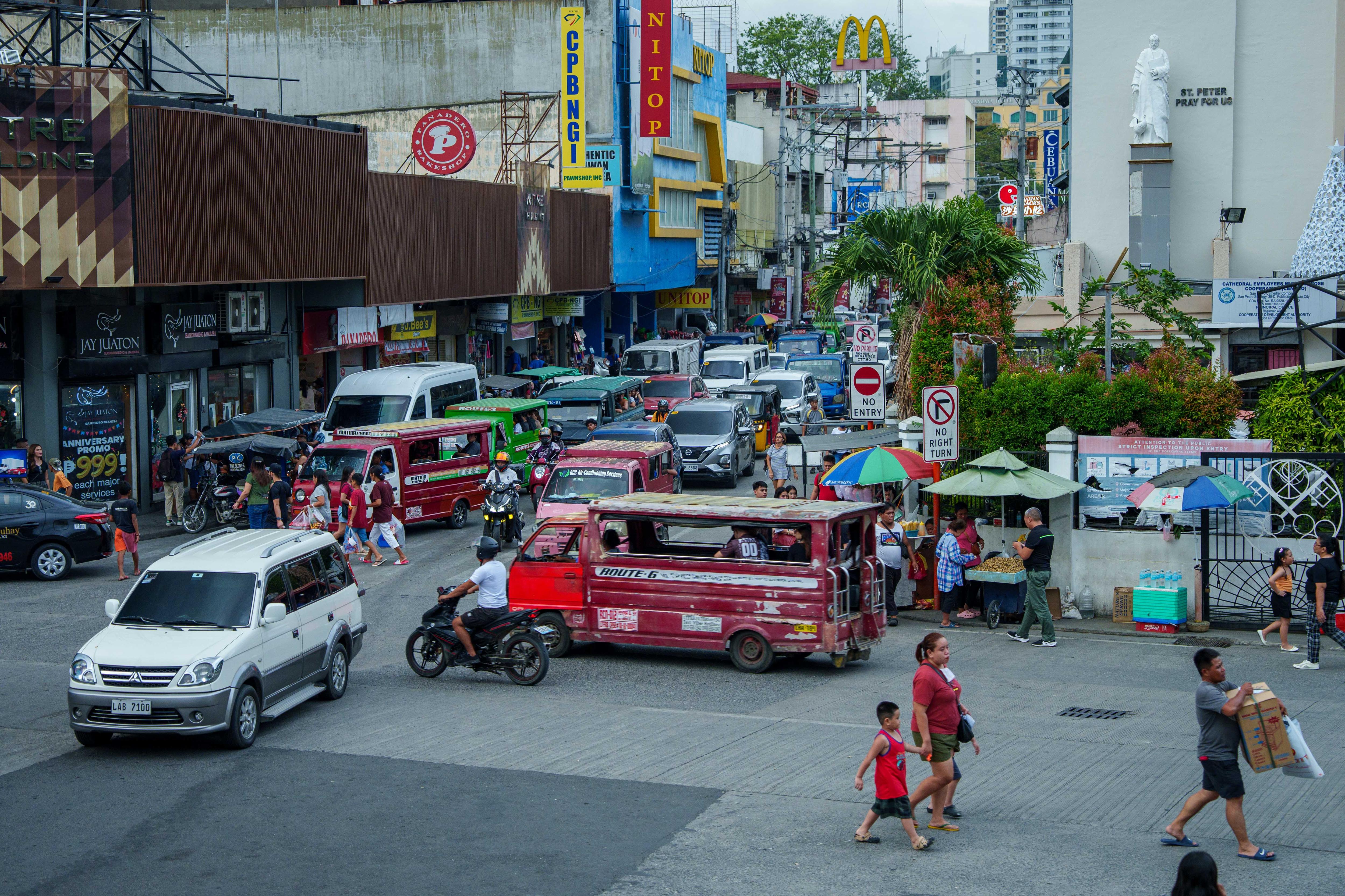 Veículos e pessoas circulam em praça pública.