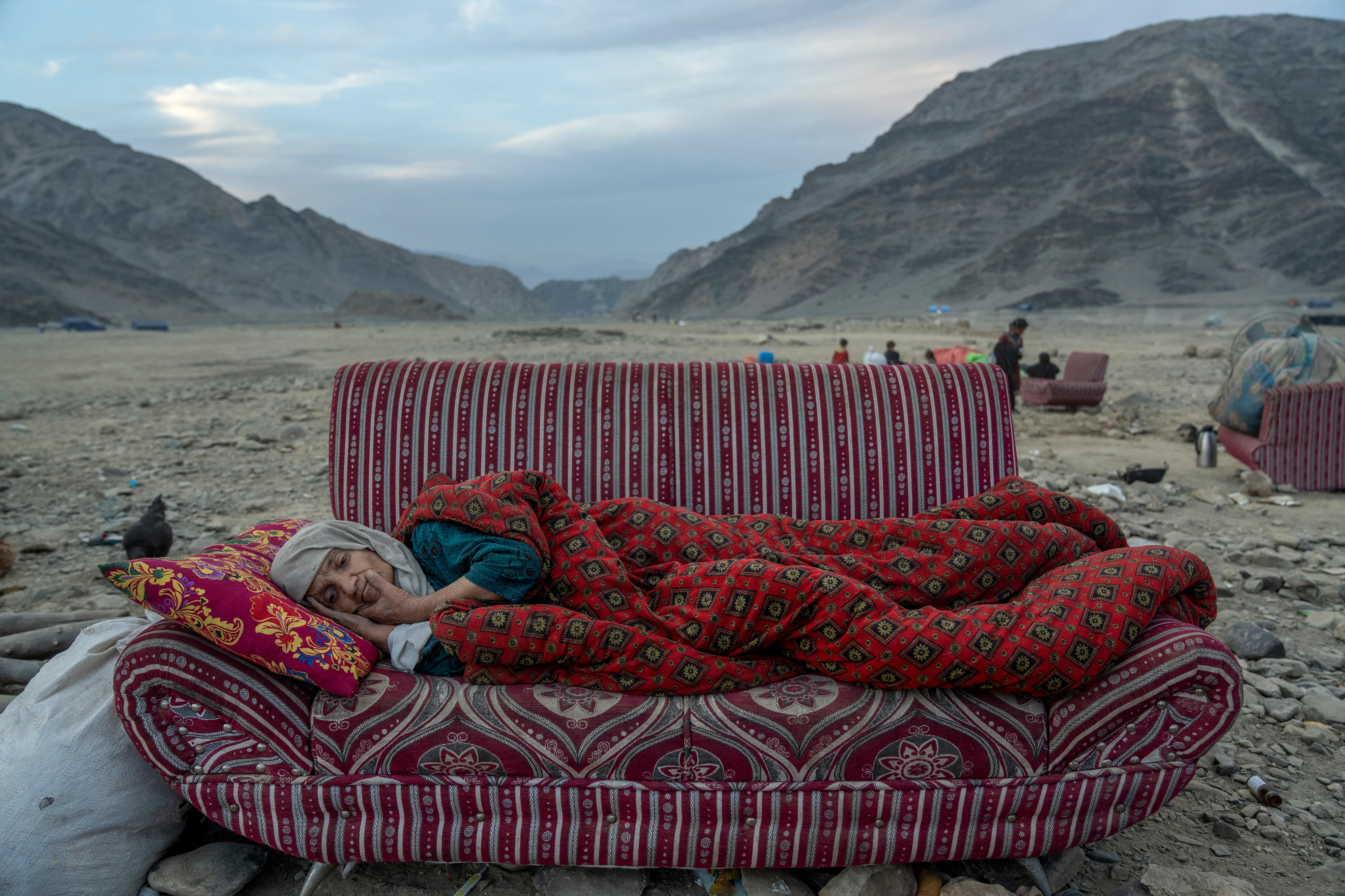 A woman rests on a couch which is outside on the ground, with desert mountains behind her