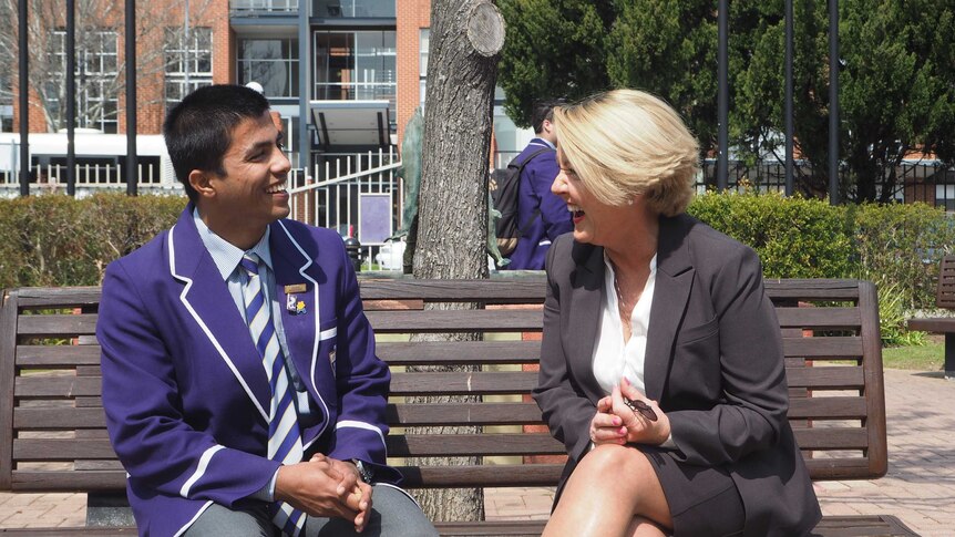 A teenage boy in a school uniform sits on a bench with the school's counsellor