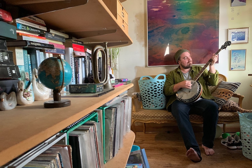 Harry Hook playing banjo in lounge next to bookcase