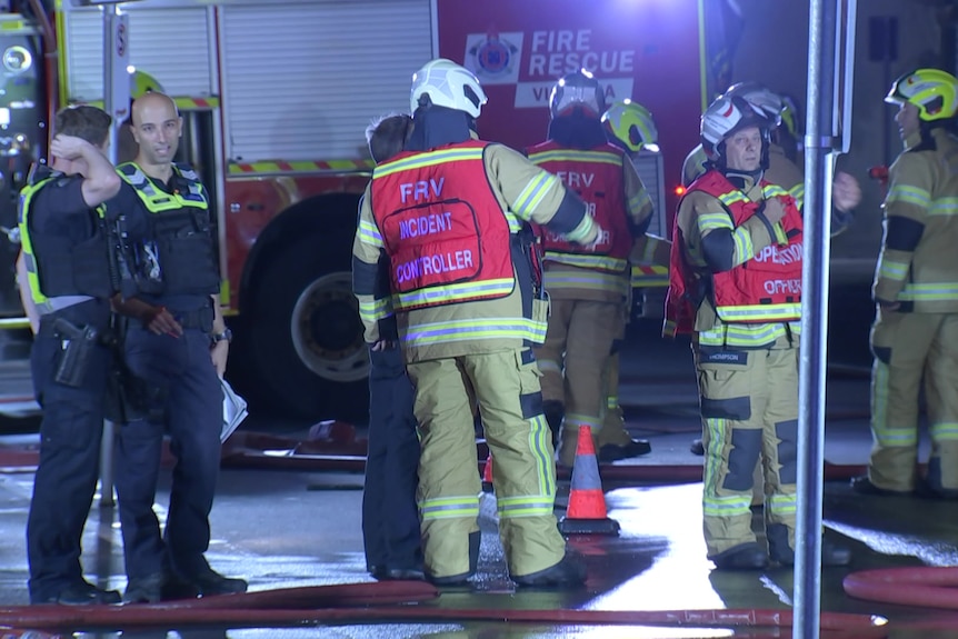 Firefighters and police at a fire scene at night.