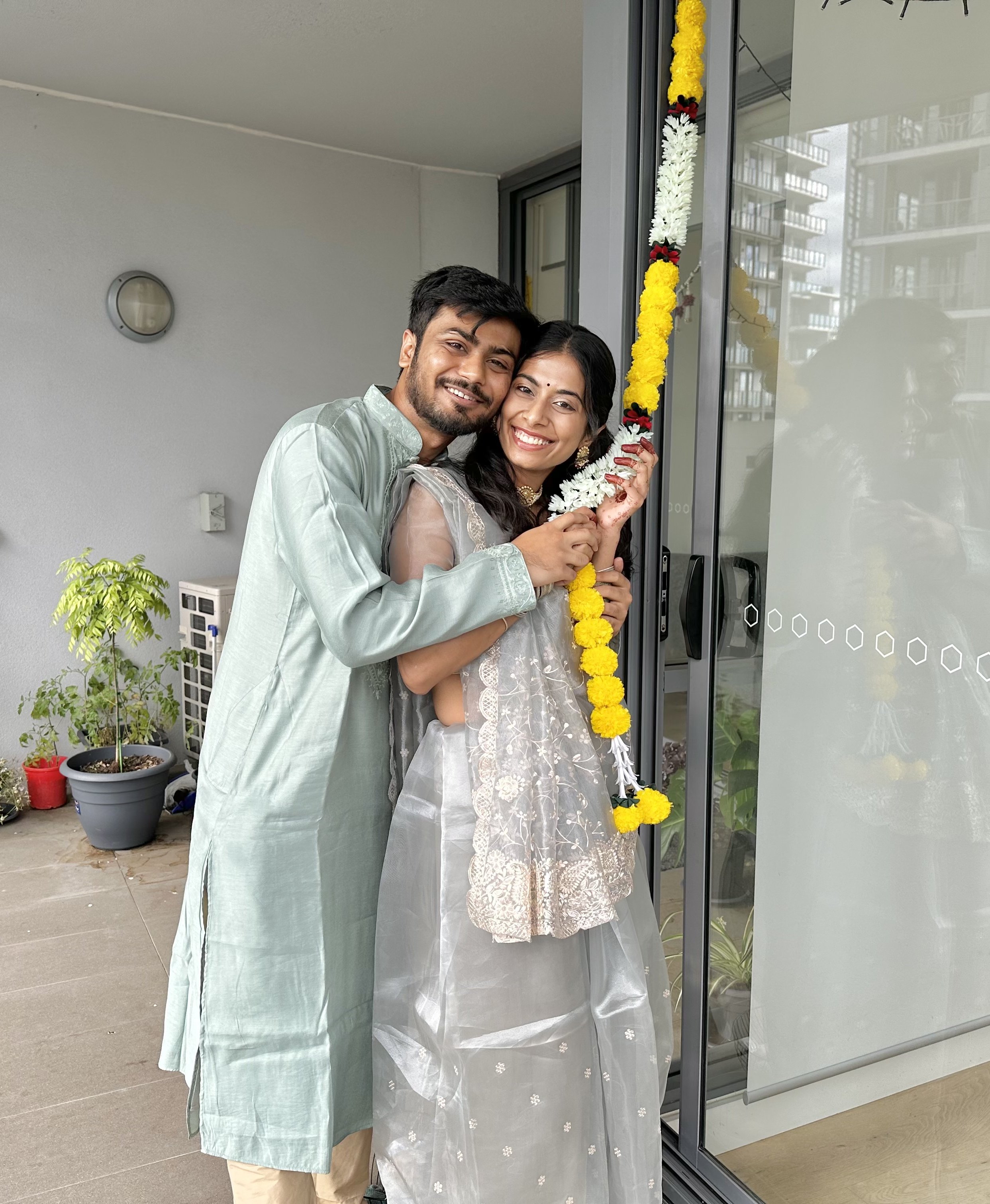 A young couple hold a string of flowers while smiling at the camera