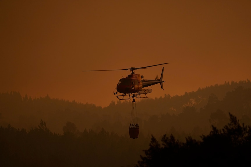 Un hélicoptère de lutte contre les incendies vole bas à travers l'épaisse fumée d'un incendie de forêt dans le village de Portugal.