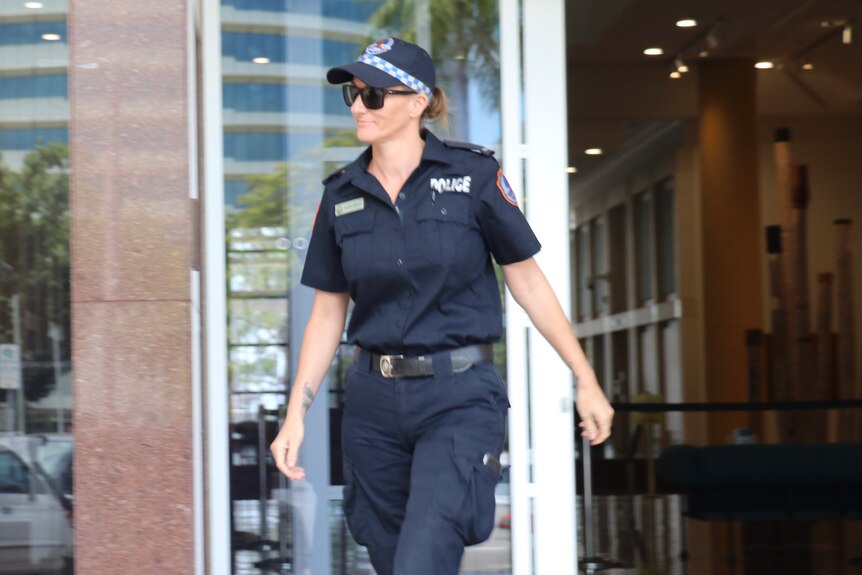 A woman wearing a police uniform and sunglasses walking out of the Supreme Court of the Northern Territory.