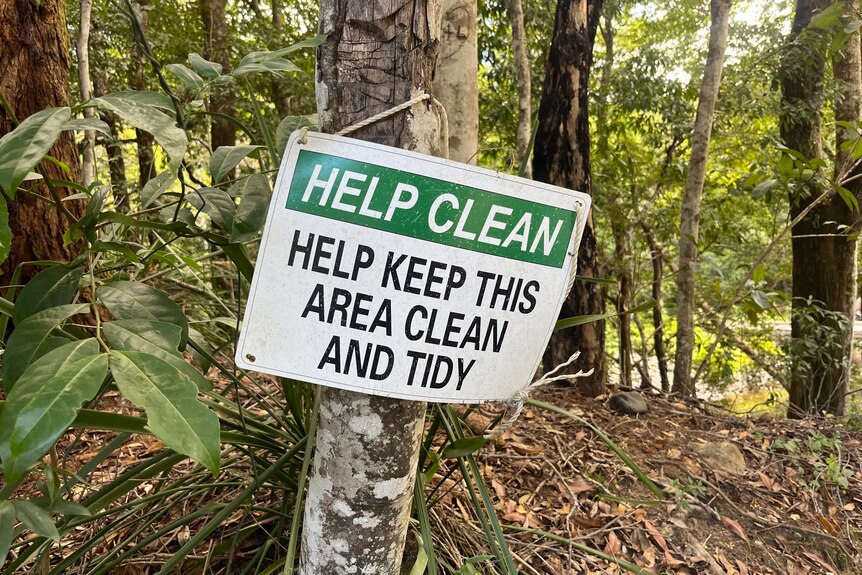 Sign hanging off a tree says 'help clean, help keep this area clean and tidy'