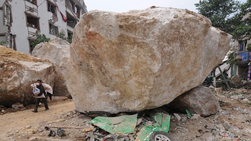 A flattened taxi lies under one of the boulders that crushed it in Sichuan Province, China