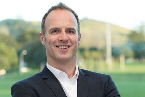 a man wearing a suit smiles at the camera while folding his arms