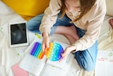 Teenage girl playing with rainbow pop-it fidget toy while studying at home