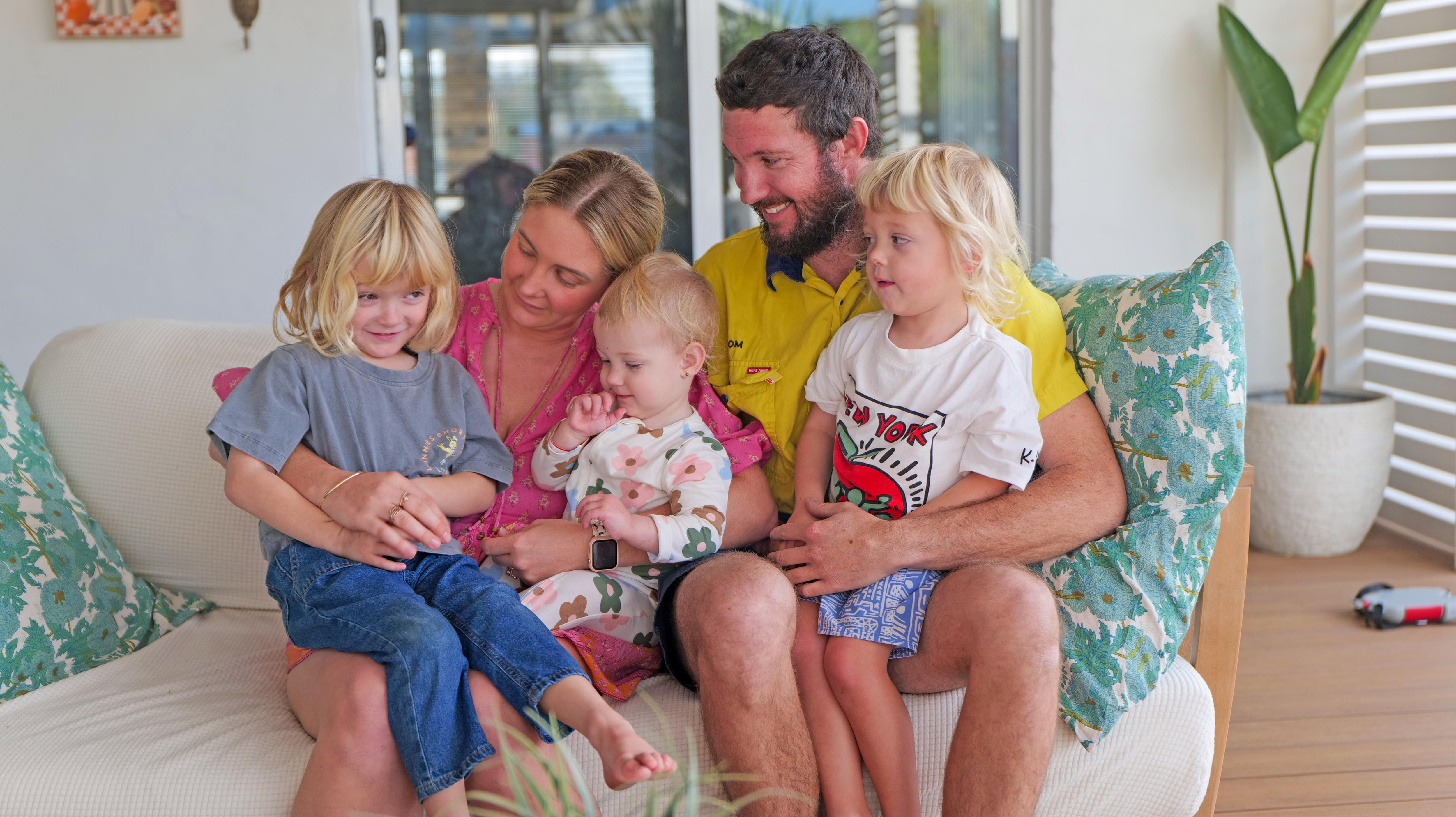 Woman and man sit on lounge with three children under five years