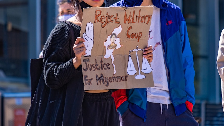 A woman holds up a sign saying 'Reject military coup. Justice for Myanmar'.