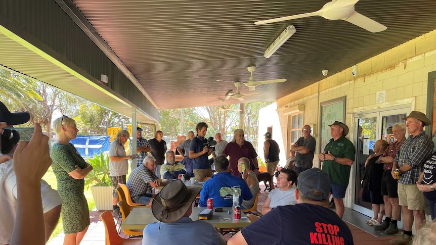 A large group of Menindee locals gathered under a shaded building space, with one man speaking to the assembled group