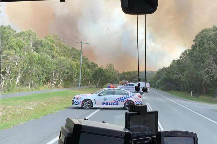 Police block a road at Peregian Beach with smoke in the background.