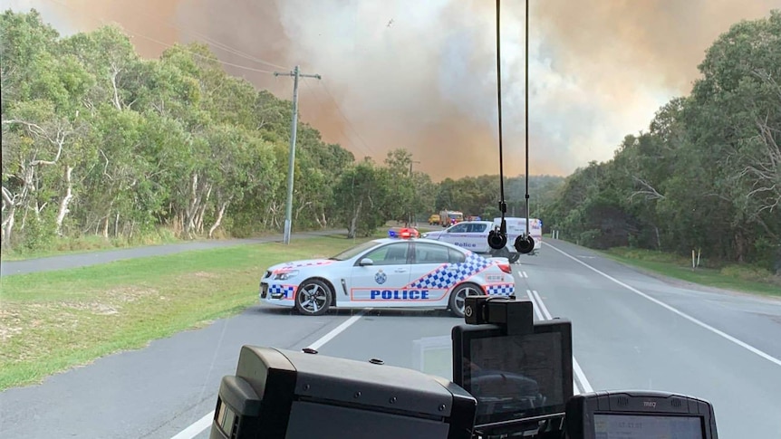 Police block a road at Peregian Beach with smoke in the background.
