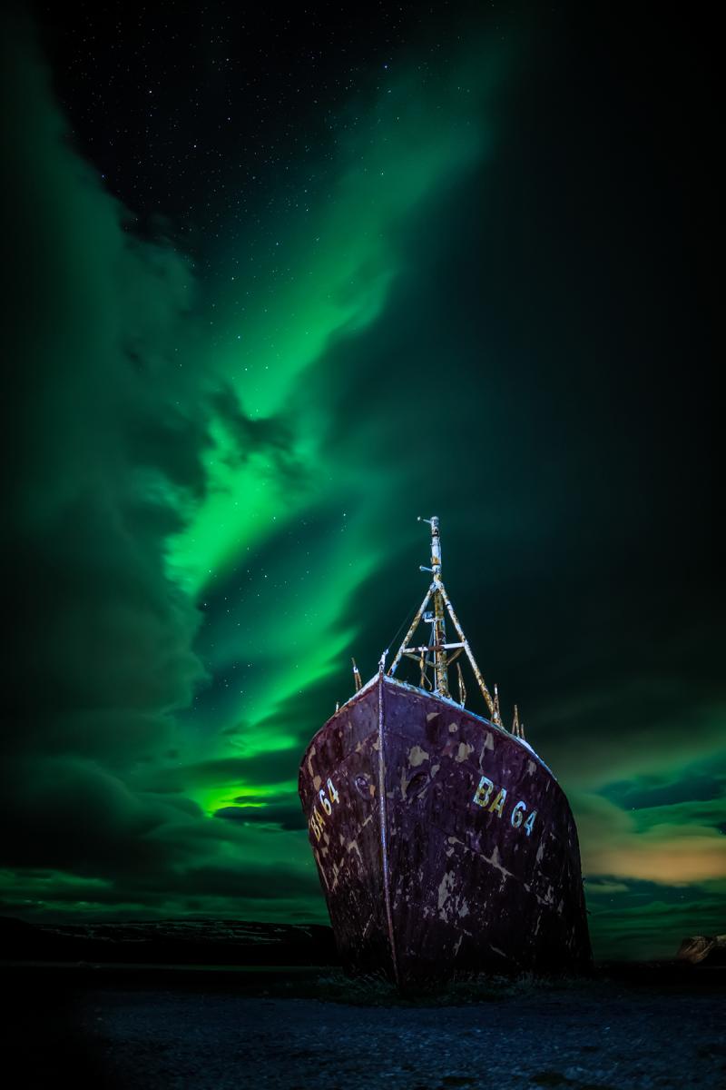 A green aurora behind a boat. 