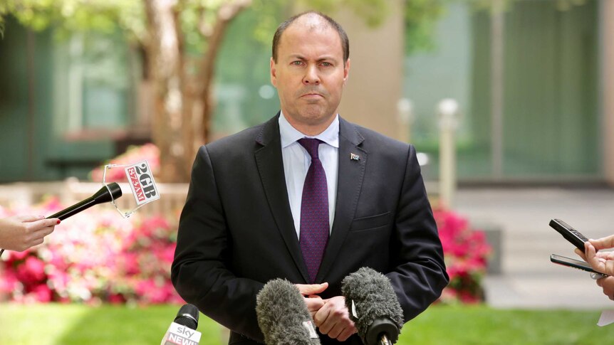Mr Frydenberg stands behind a microphone stand in one of Parliament House's courtyards.