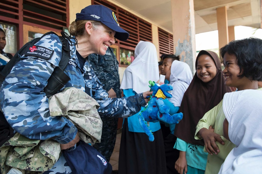 RAAF corporal smiles while she gives plush blue toy to Indonesian student