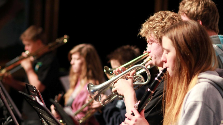 Students playing woodwind and brass instruments in a pit band.