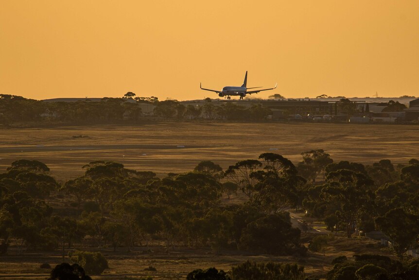 A jet aircraft on final approach landing at sunset.  