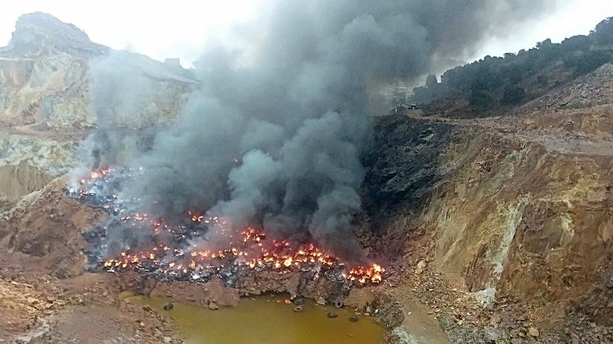 Thousands of tyres on fire and lots of smoke in a gully at a mine site.