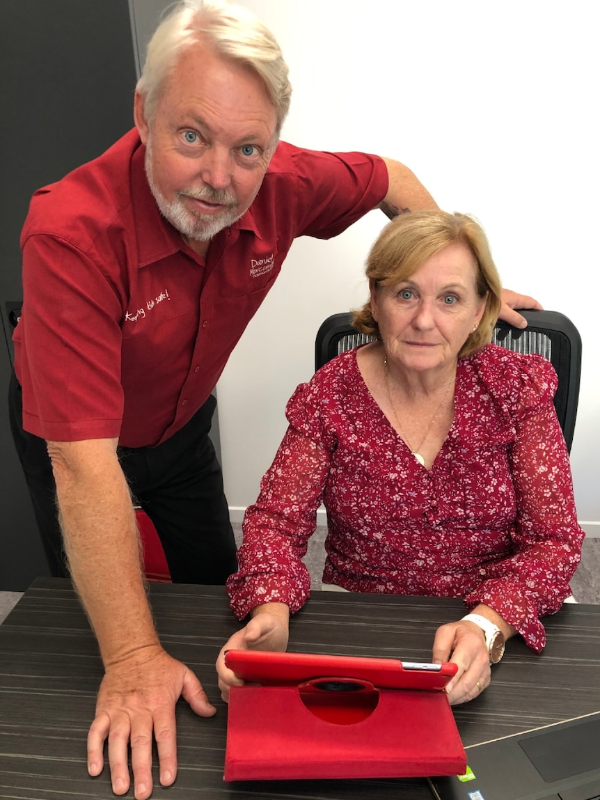 A man and woman stand over a tablet computer.