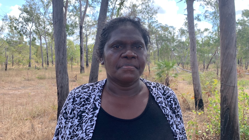 An Aboriginal woman standing in savannah scrub, looking past the camera.