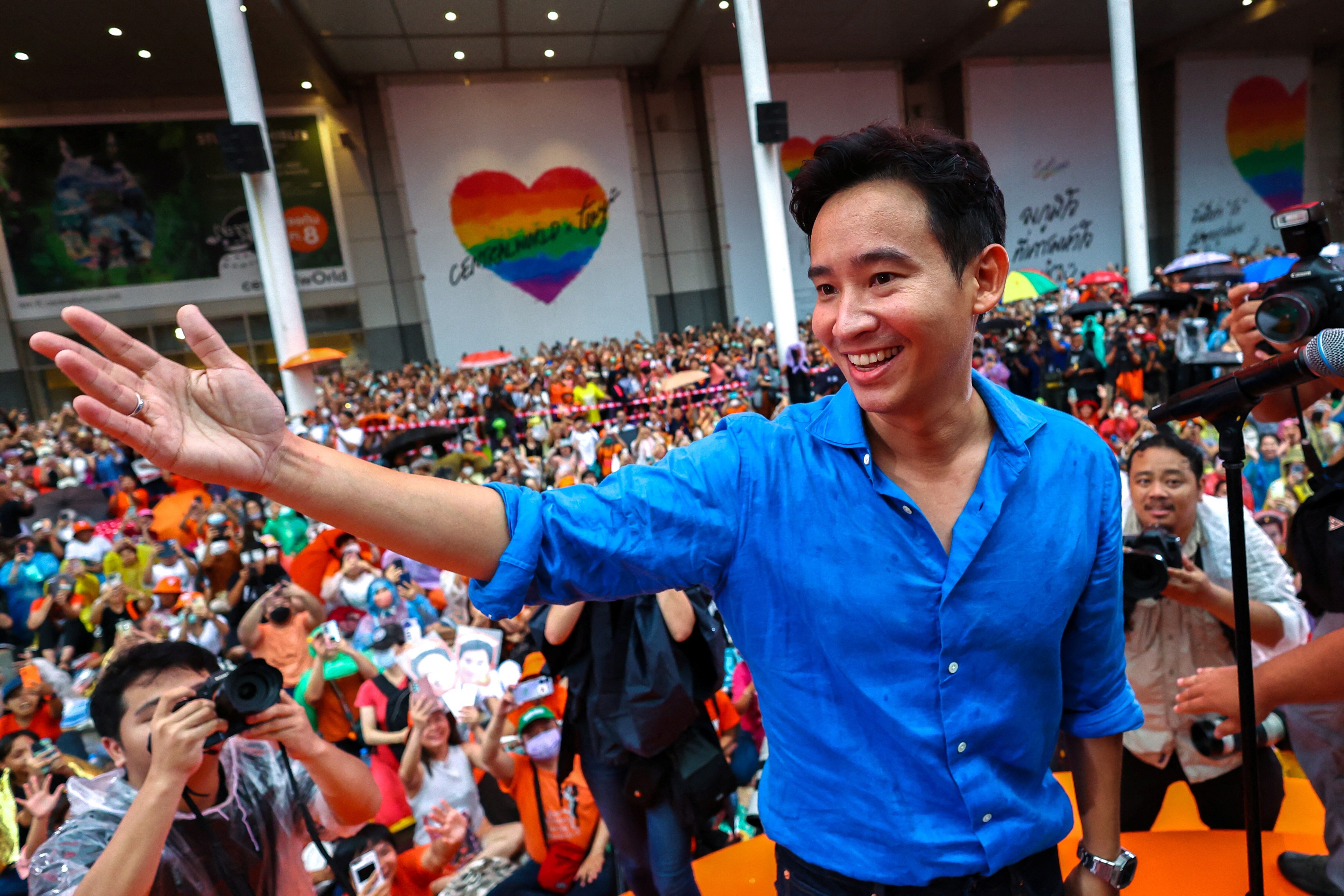 A young, smiling Thai man in a blue shirt speaks in front of thousands.