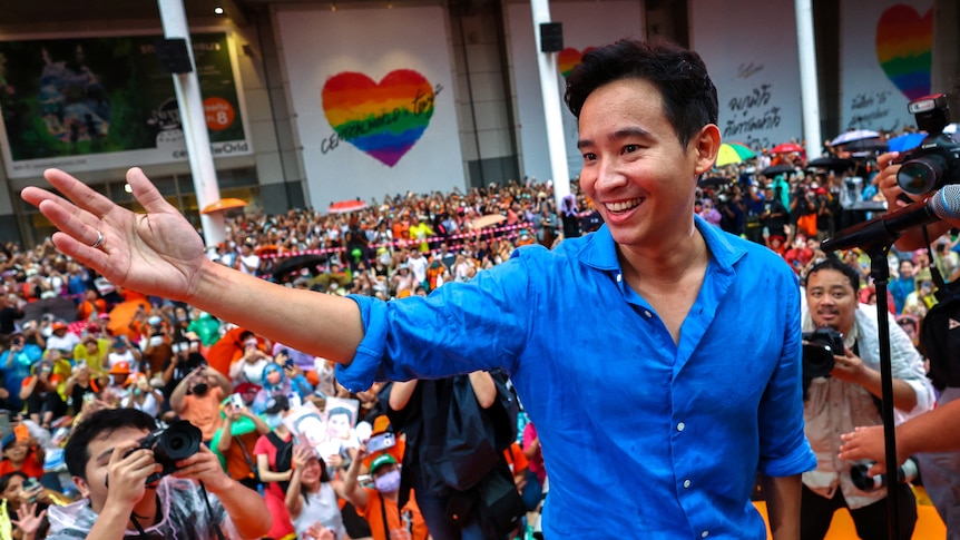 A young, smiling Thai man in a blue shirt speaks in front of thousands.