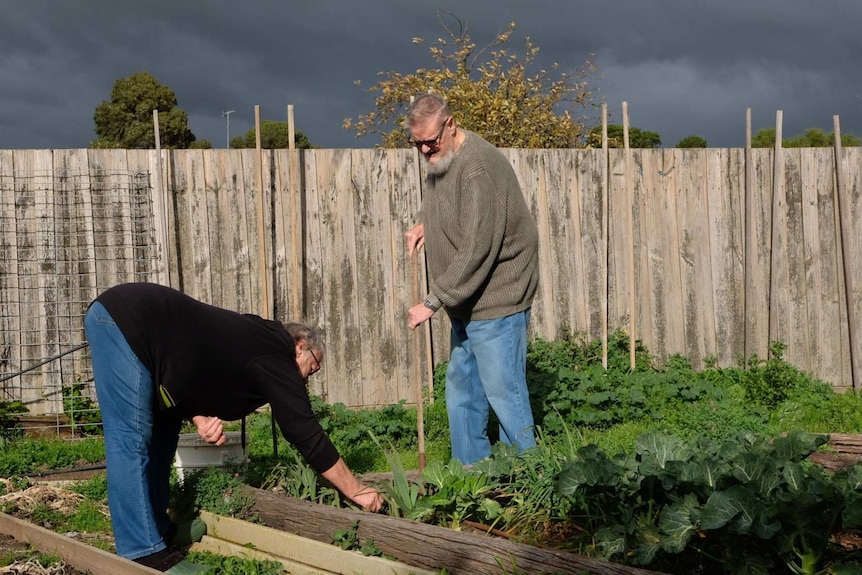 Stuart Leamer stands with a rake in his hand, while Tammy Leamer bends over to pull out weeds.