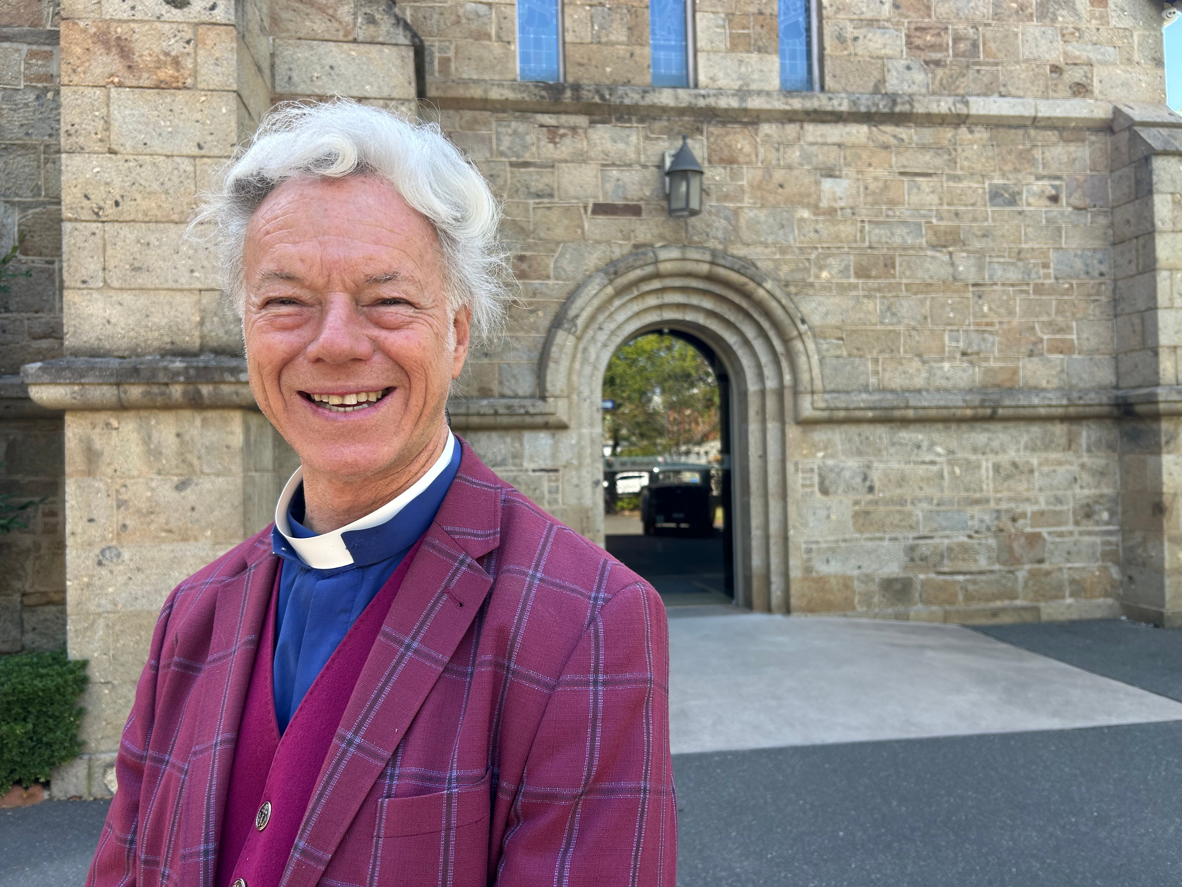 un sacerdote con traje morado frente a una iglesia 