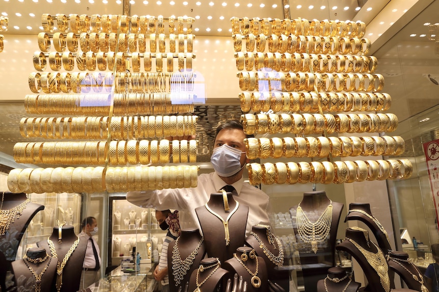 A goldsmith wearing a protective face mask arranges golden bangles as the other talks to customers.
