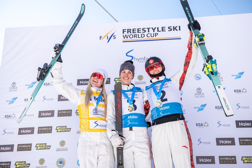 Trois femmes se tiennent souriantes tenant leurs skis