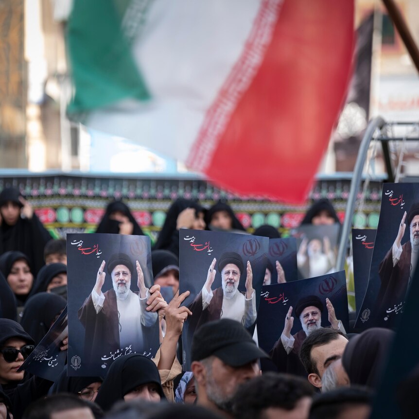 crowd holding up portraits of Iranian President Ebrahim Raisi, and an Iran flag