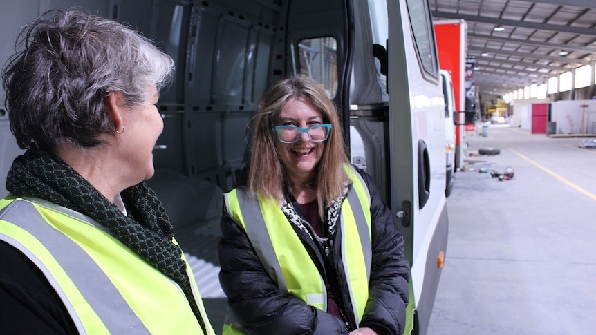 Two women, Sally Goldstraw and Elizabeth Jewson from WRISC in Ballarat, sit next to a van.
