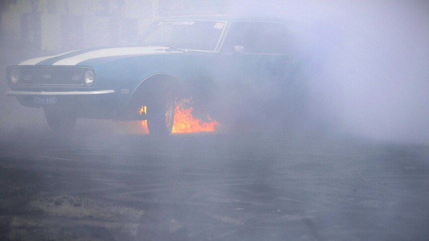 Fire burns under a car as it performs a burnout during Summernats.