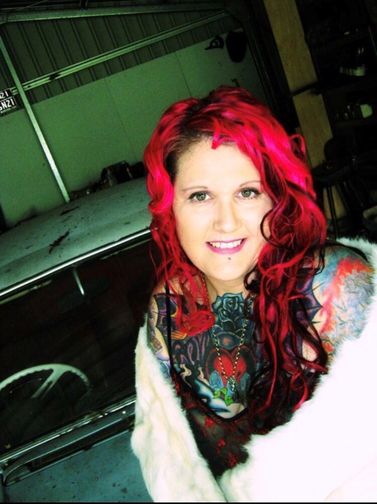 A woman with bright pink hair and large, colourful tattoos smiling