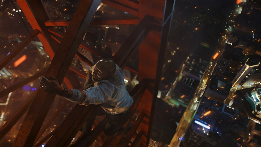 Still image from 2018 film Skyscraper of Dwayne Johnson hanging from a construction structure high above a cityscape.