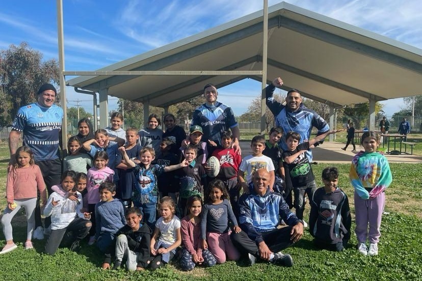 A group of school children at the Wilcannia Central School posing with former NRL players on an oval.  