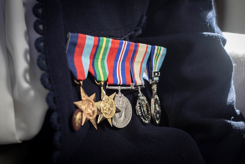 Five war medals pinned to a woman's navy cardigan.