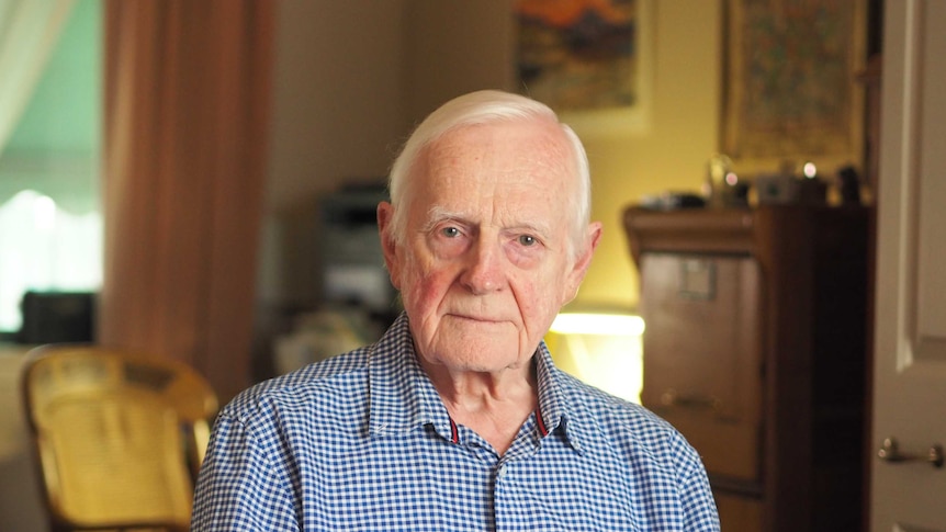 An elderly man looks at the camera while sitting in his living room